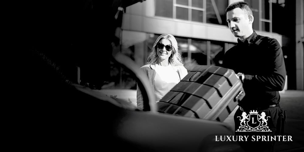 Businesswoman standing beside a luxury vehicle while chauffeur loads suitcase into the boot, representing premium executive travel service.